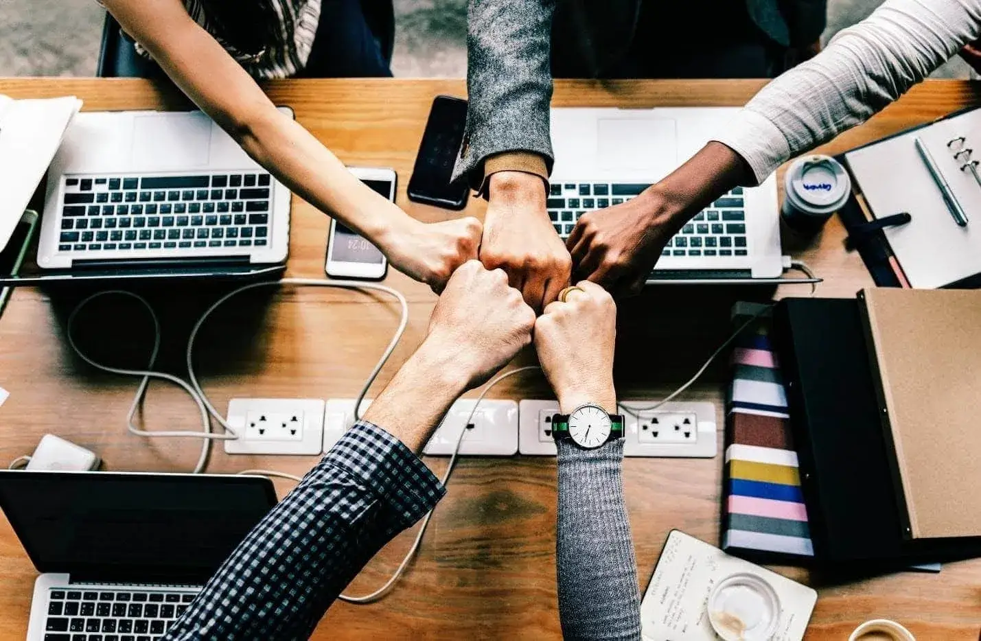 Four people fist-bumping over a table with laptops and notebooks.