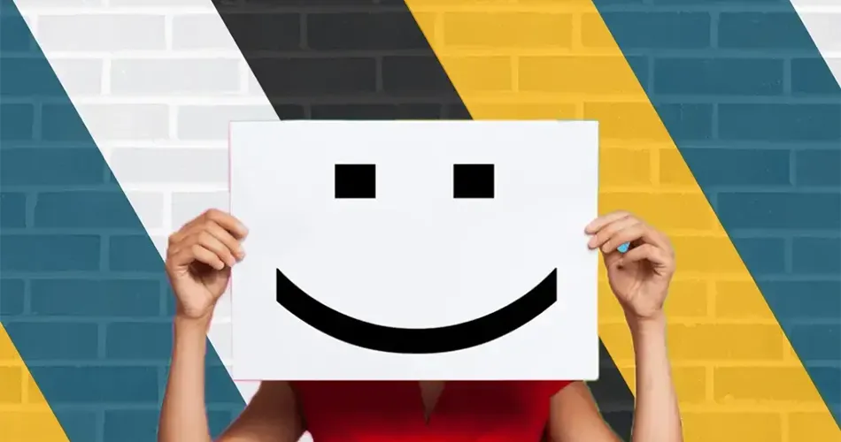 A woman holds up a smiley face paper against a brick wall. Affordable social media management